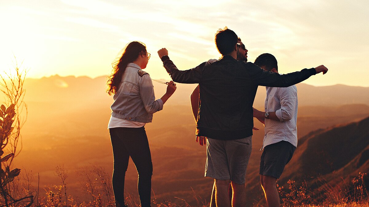 Zu sehen sind drei junge Menschen, die befreit im Sonnenuntergang tanzen.